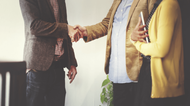 3 professional speaking together, two shaking hands.